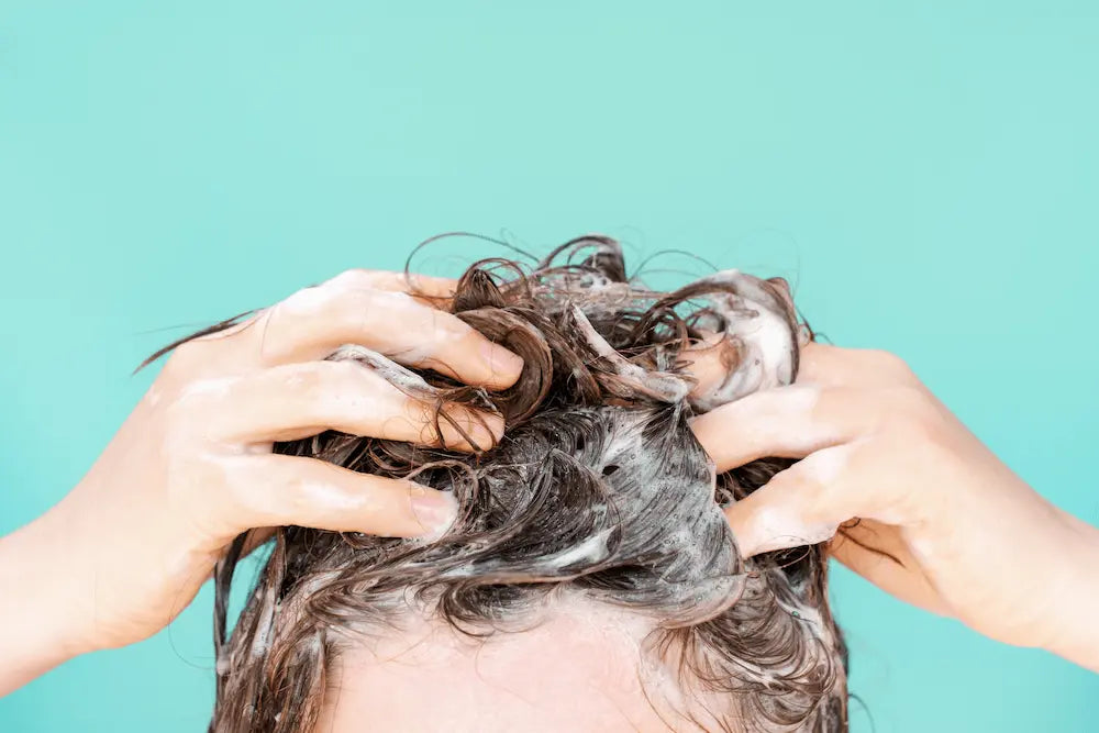 A woman washes her hair with shampoo on mint background, front view